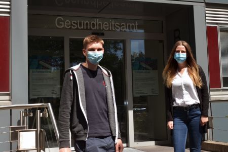 zu sehen sind die beiden Auszubildenden vor dem Eingang des Gesundheitsamtes